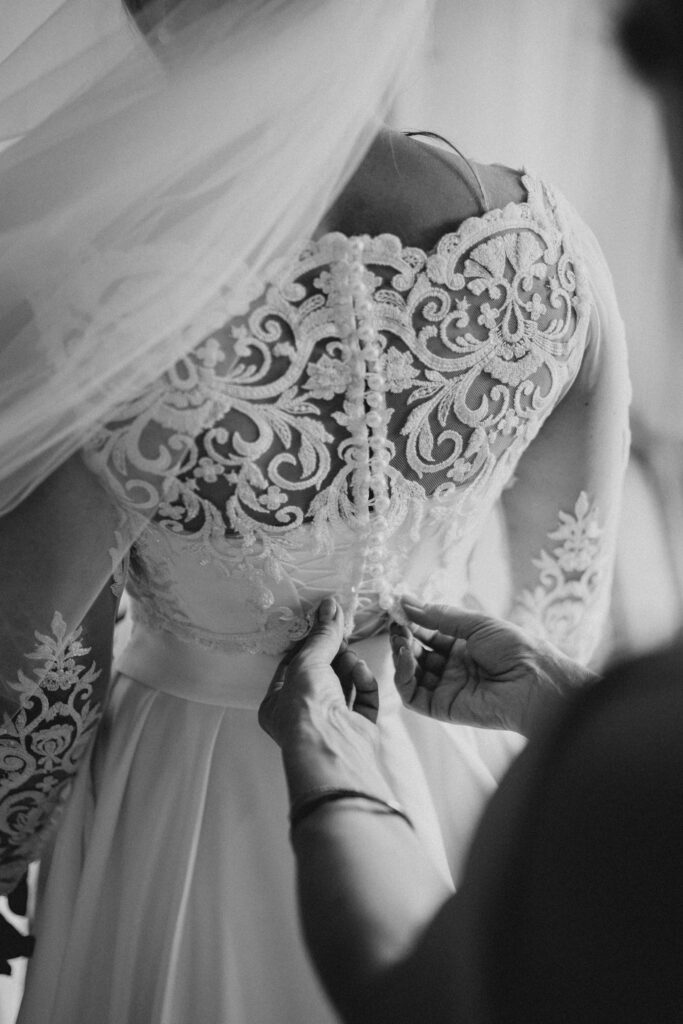 Braut wird beim Getting Ready das Kleid zugeknöpft